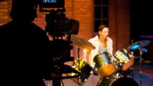 A drummer in the background lit with orange lights and a camera man silhouetted in the foreground